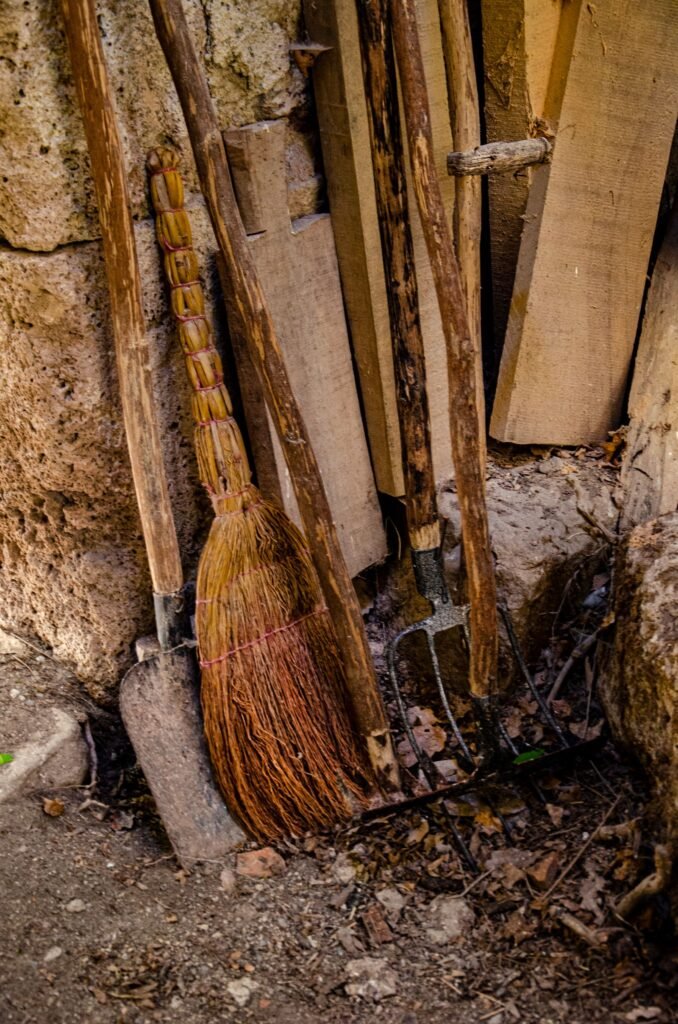 Bezems en harken tegen een houten wand, op te bergen in een kunststof tuinkast van brico voor bezems
