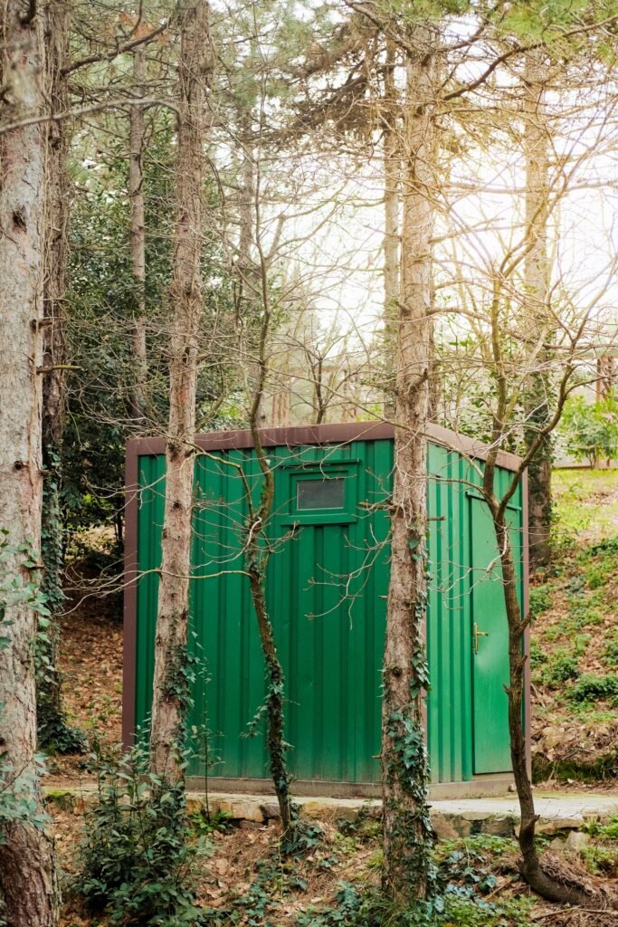 Groene metalen berging tussen de bomen in een bosrijke tuin, voorbeeld van een metalen tuinkast
