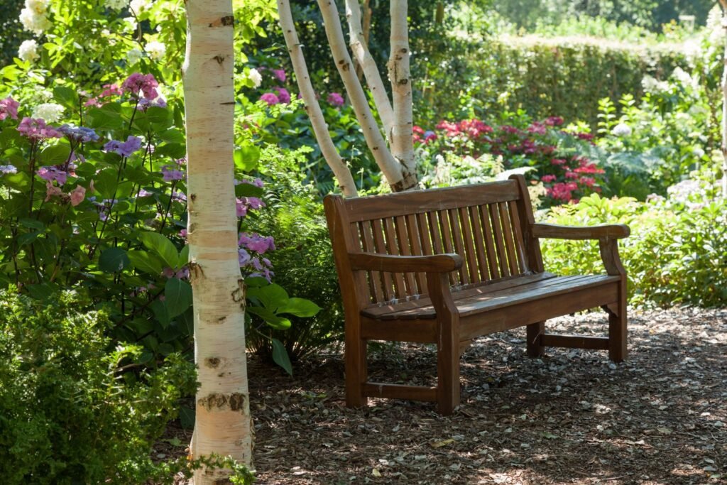 Houten tuinbank tussen de bloemen in een groene tuin, in dezelfde stijl als een tuinkist hardhout