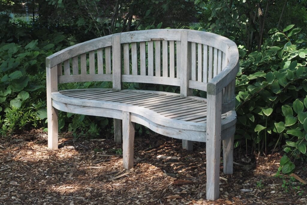 Gebogen houten tuinbank tussen het groen, hout zoals bij een tuinkist hardhout of douglas