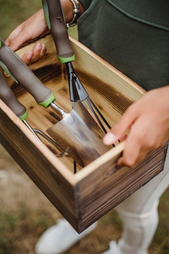 Hand die tuingereedschap uit een houten kist haalt, voorbeeld van een kleine tuinkist hout